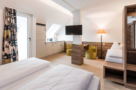 Blick in das Zimmer der Panoramasuite im Hotel Zach: Doppelbett, Einzelbett, Sitzgelegenheit, Küche, Tür zur Terrasse
