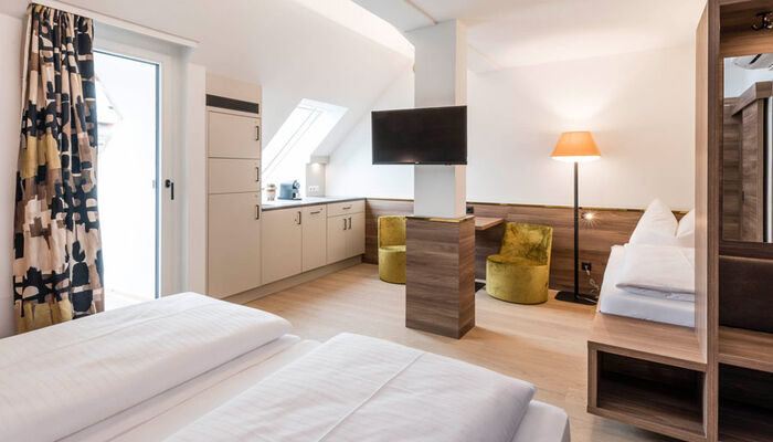 Blick in das Zimmer der Panoramasuite im Hotel Zach: Doppelbett, Einzelbett, Sitzgelegenheit, Küche, Tür zur Terrasse